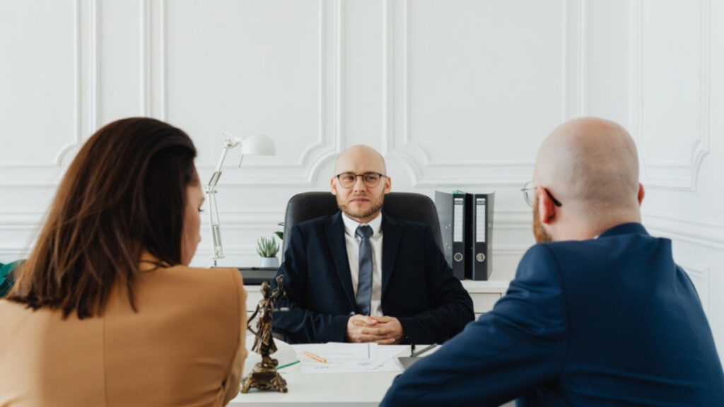A couple sitting together across the desk from their attorney during a planning meeting