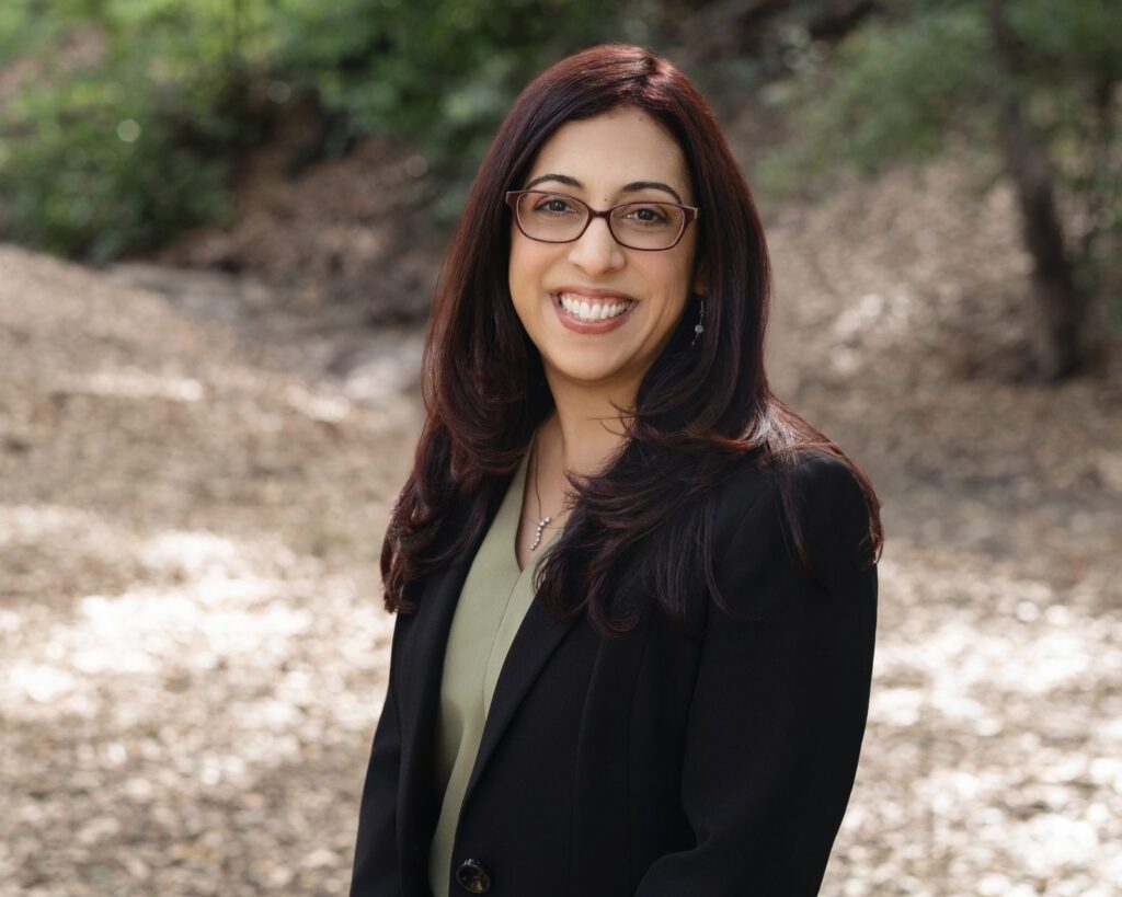 Estate planning attorney Marissa Garcia in a black blazer and glasses, photographed outdoors among trees