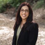 Estate planning attorney Marissa Garcia in a black blazer and glasses, photographed outdoors among trees