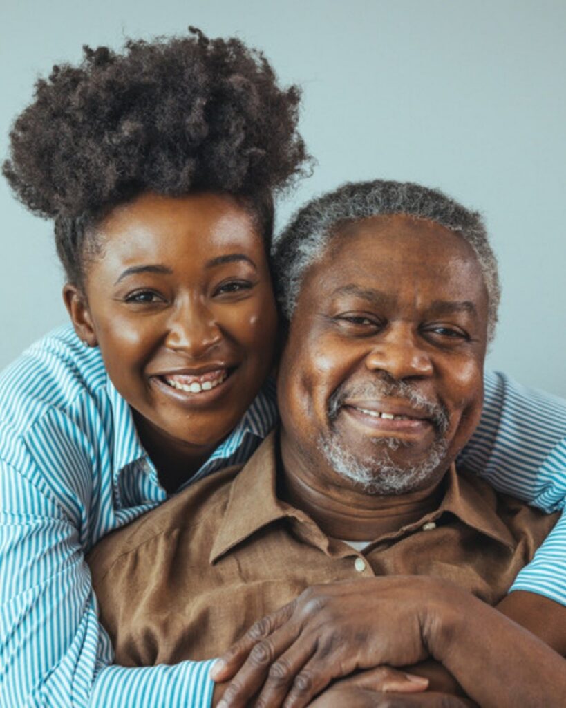 An adult daughter hugging her smiling elderly father