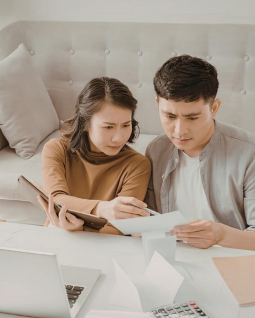 Two adults reading through paperwork on a sofa with a laptop and calculator on the table