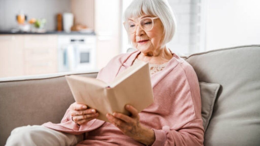 An older woman reading a book alone on her living room sofa