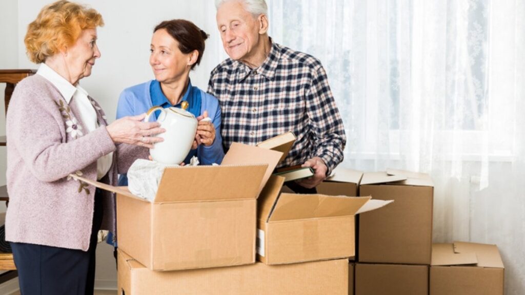 An older couple packing kitchen items into moving boxes with help from a younger woman