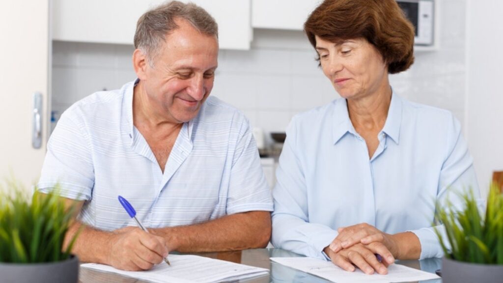 An older couple signing papers at their kitchen table, the kind of plan estate planning and trust attorneys in Ventura County prepare