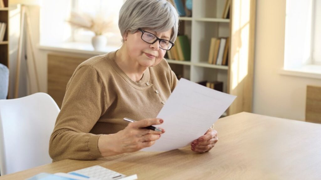 A woman reviewing statements at her dining table with a pen in hand